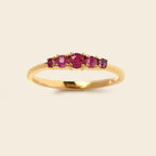 A yellow gold ring featuring five round-cut pinkish-red gemstones set across the top, presented on a light beige background.