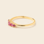 A gold ring featuring a curved row of small round pink gemstones on the front, photographed on a plain light beige background.