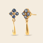 A pair of gold dangle earrings with a cluster of round blue gemstones at the top and a teardrop-shaped gold drop below, shown on a light beige background.