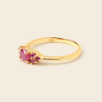 A yellow gold ring featuring a large oval pink gemstone and two smaller round-cut pink gemstones, set in a polished gold band against a light beige background.