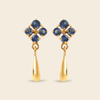 A pair of gold dangle earrings featuring a cluster of round blue gemstones at the top and a teardrop-shaped gold drop below, set against a solid light beige background.