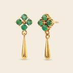A pair of gold dangle earrings featuring a four-stone green gemstone floral cluster on the top and a polished gold teardrop drop below, set against a solid light beige background.