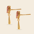 A pair of gold drop earrings with a stacked rectangular cluster of small pink gemstones and a teardrop-shaped drop, shown on a light beige background.