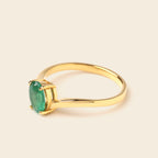 A gold ring with a round green gemstone in a prong setting, shown on a light beige background.
