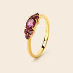 A yellow gold ring featuring a oval-cut pink gemstone in the center, accented by smaller round pink gemstones on the shoulders, set against a solid light beige background.