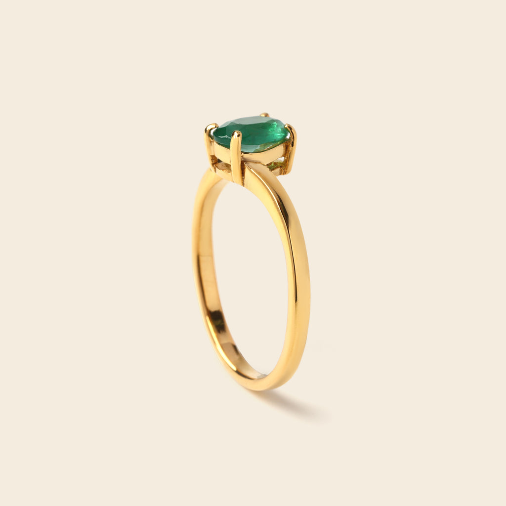 A gold ring with a oval-cut green gemstone in a prong setting, shown on a light beige background.