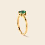 A gold ring with a oval-cut green gemstone in a prong setting, shown on a light beige background.