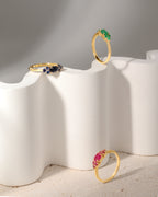 Three gold rings displayed on a sculptural white pedestal against a soft gray background. 