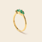 A gold ring featuring a cluster of green gemstones, photographed on a clean, solid, light beige background.
