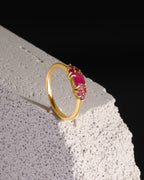 A gold ring with a cluster of oval pink gemstones, displayed on a textured white stone block against a solid black background.