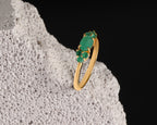 A gold ring with a cluster of green gemstones, displayed on a textured white stone against a solid black background.