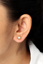 A close-up of a person's ear wearing a small gold stud earring with a clear faceted gemstone.