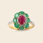 A yellow gold ring featuring a central oval pinkish-red gemstone surrounded by a halo of green oval gemstones, with a band set with small clear stones, shown on a light beige background.