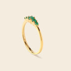 A gold ring featuring a curved row of small green marquise-cut gemstones on a plain, light beige background.