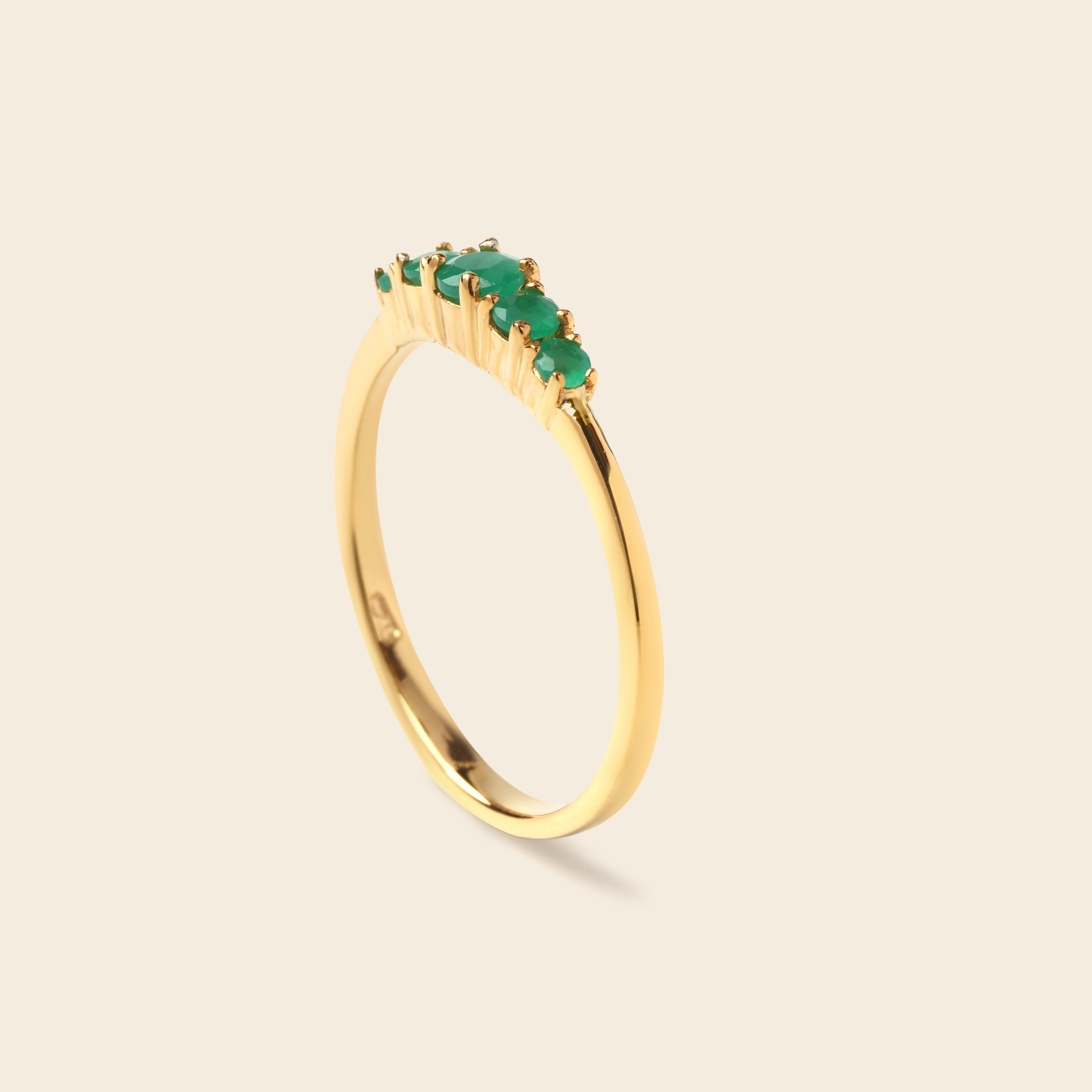 A gold ring featuring a curved row of small green marquise-cut gemstones on a plain, light beige background.