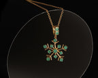A gold snowflake pendant necklace with green gemstone accents, displayed on a clear circular stand against a black background.