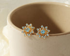 Flower-inspired blue topaz gemstone studs in gold — pair view