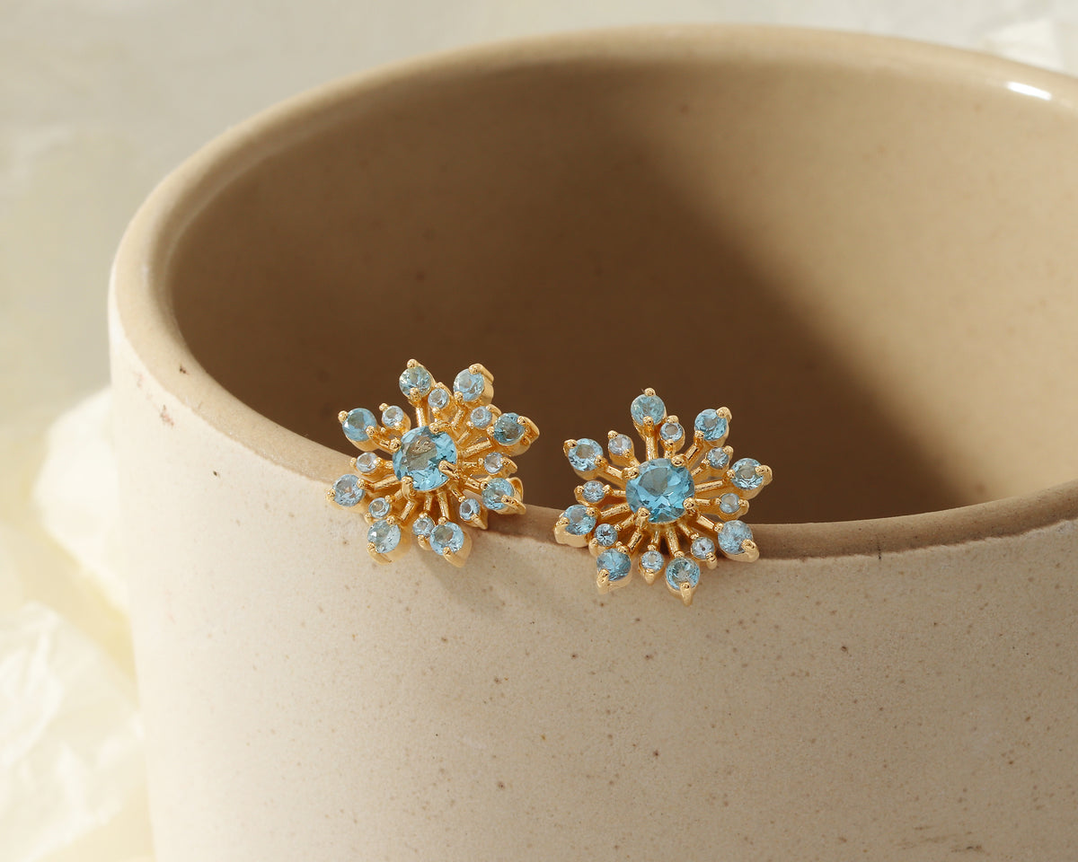 Flower-inspired blue topaz gemstone studs in gold — pair view