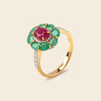 A yellow gold ring featuring a central oval pinkish-red gemstone surrounded by a halo of green oval gemstones, with a pavé-set silver band adorned with small clear stones.