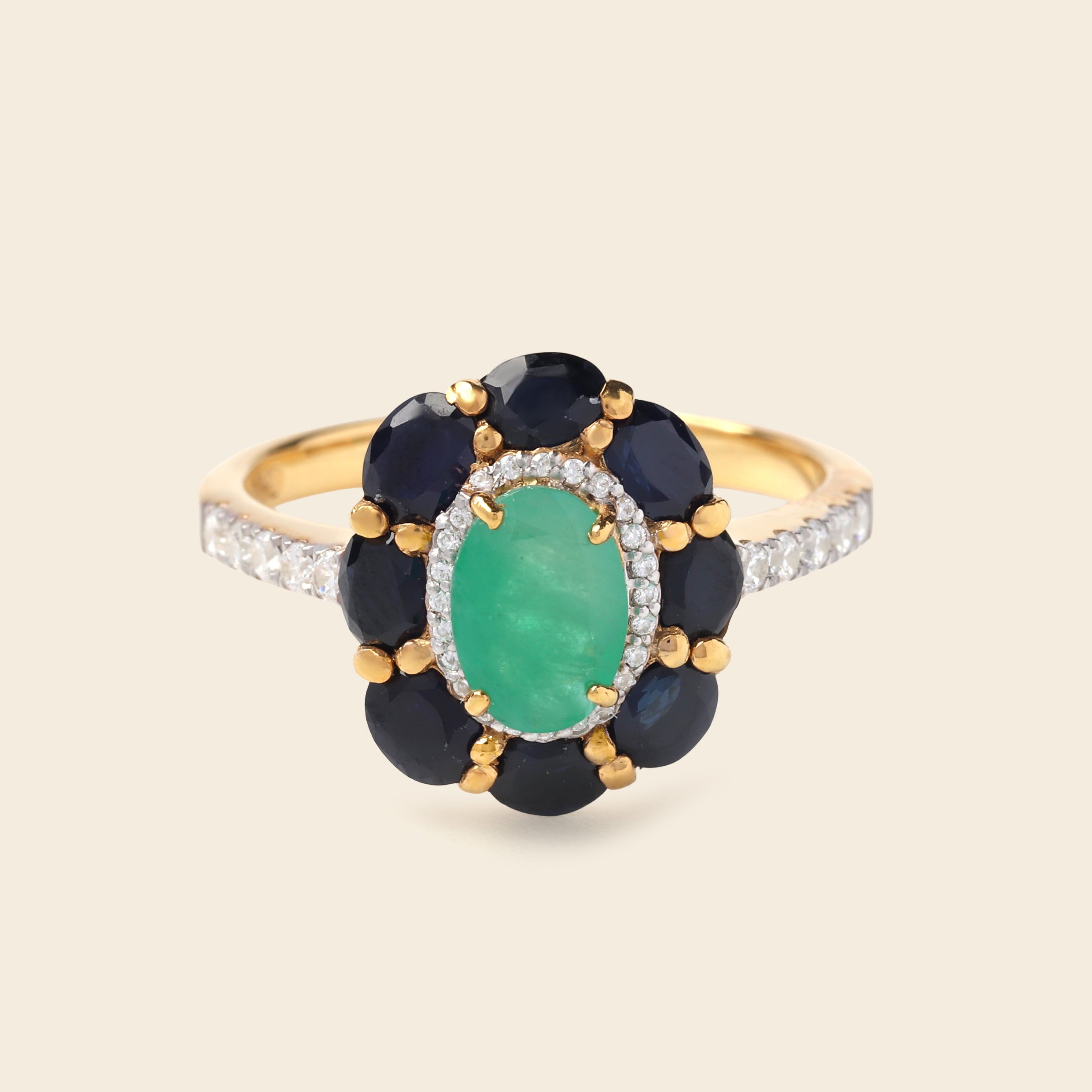 A yellow gold ring featuring a central oval green emerald-cut stone surrounded by a halo of round dark blue sapphires and small clear accent stones on a light beige background.