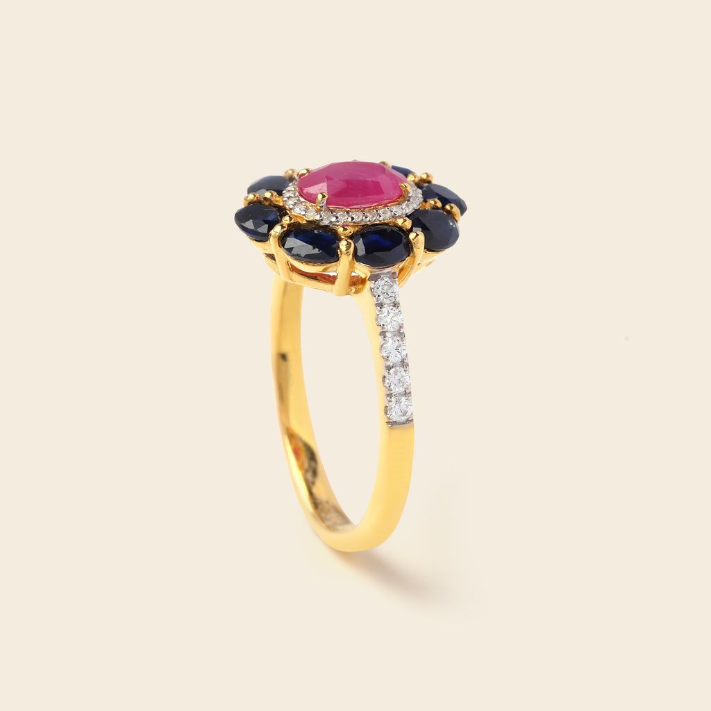 A yellow gold ring featuring a central oval pink gemstone surrounded by a halo of dark blue oval gemstones, with a pavé band set with small clear stones, shown on a light beige background.