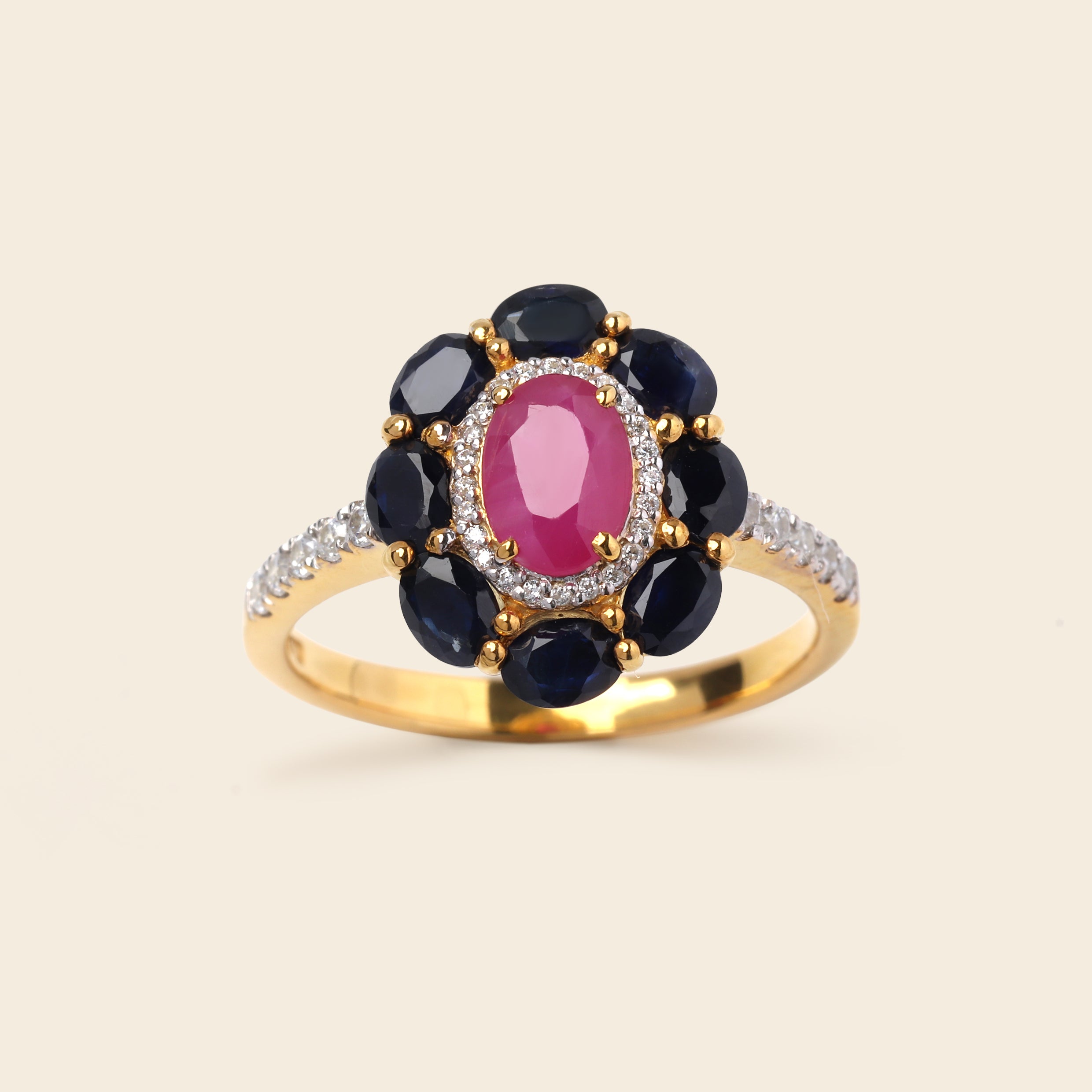 A yellow gold ring featuring a central oval pink gemstone surrounded by a halo of dark blue gemstones, with a diamond-accented band, set against a light beige background.