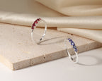 Two slim silver rings displayed on a beige stone slab with draped cream satin fabric in the background.