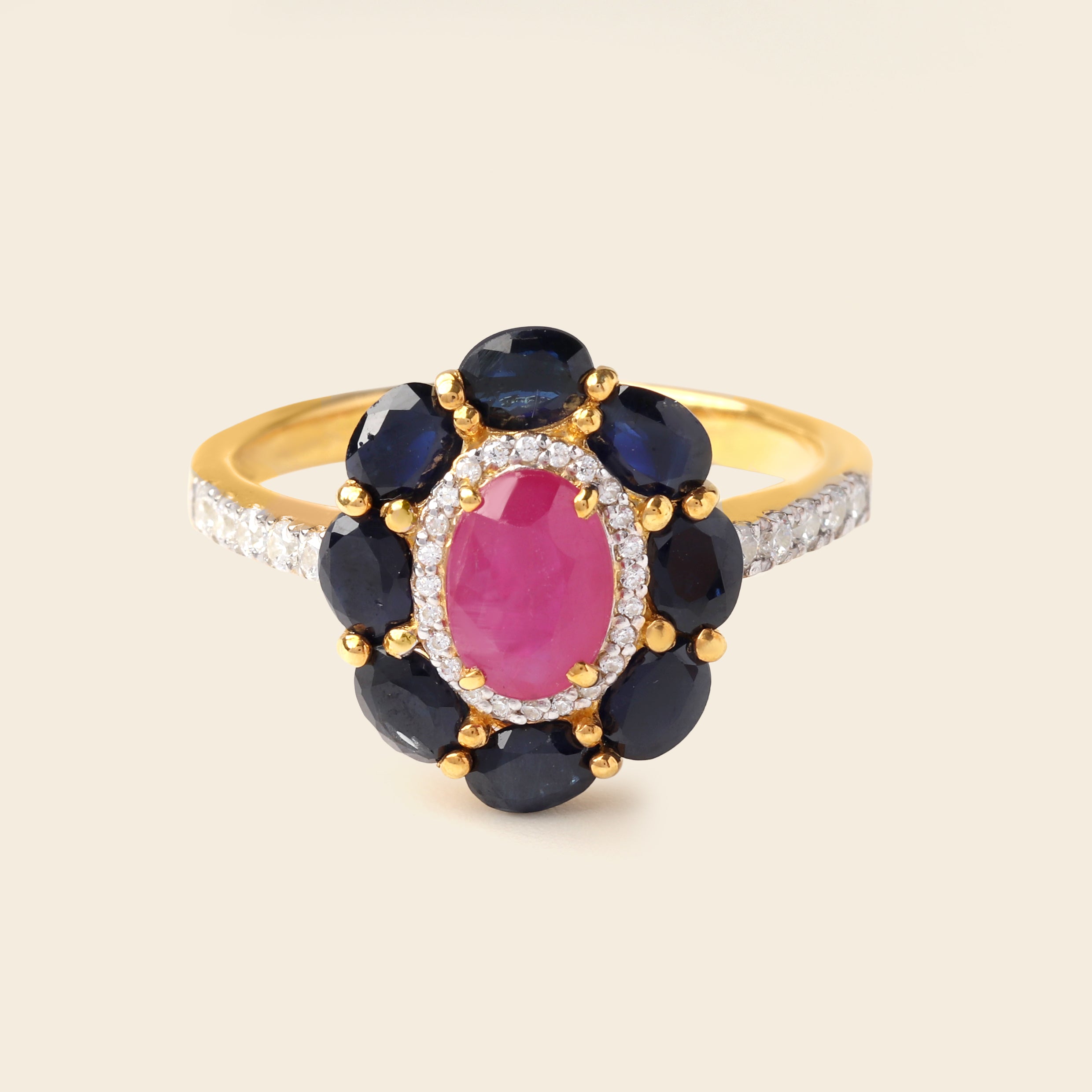 A yellow gold ring featuring a central oval pink gemstone surrounded by a halo of dark blue round gemstones, with a diamond-accented band, set against a light beige background.