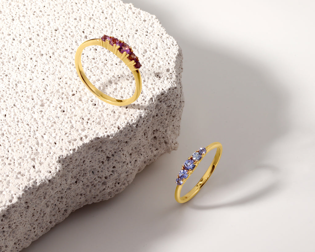 Two gold rings displayed on a white surface next to a textured stone slab. 