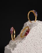 Three gold rings with colorful gemstones displayed on a textured white stone block against a solid black background.