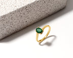 A gold ring with an oval-cut green gemstone, displayed on a clean white surface next to a textured gray stone block.