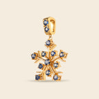 A gold snowflake pendant charm embellished with small round blue gemstones, shown against a solid light beige background.