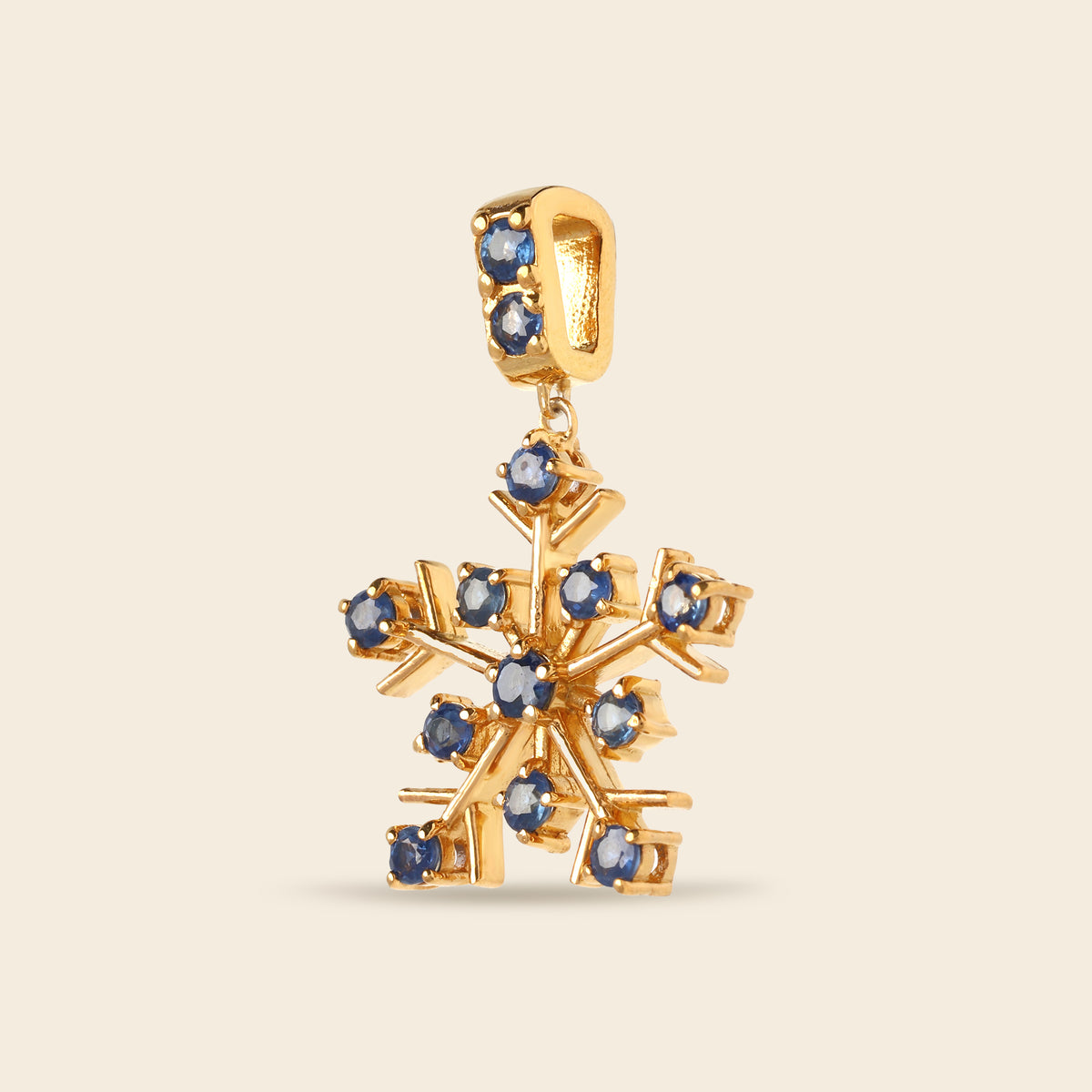 A gold snowflake pendant charm embellished with small round blue gemstones, shown against a solid light beige background.
