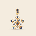 A gold snowflake-shaped pendant featuring multiple round blue gemstones, set against a solid light beige background.