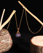 A gold chain necklace with a decorative padlock pendant, displayed on a black background with rustic wood props.