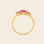 A gold ring featuring a central rectangular pink gemstone flanked by smaller round pink stones, shown against a solid light beige background.