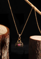 Gold necklace with a miniature handbag pendant featuring a pink oval gemstone and small gold stars, displayed against a black background with rustic wood logs.