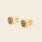A pair of gold flower-shaped stud earrings featuring a central green oval stone surrounded by small pink stones, shown on a light beige background.