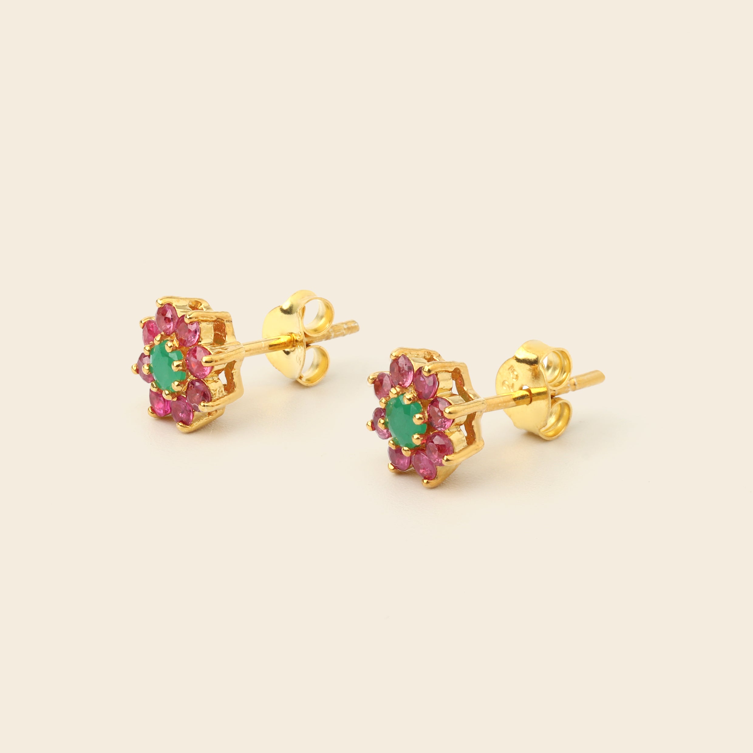 A pair of gold flower-shaped stud earrings featuring a central green oval stone surrounded by small pink stones, shown on a light beige background.