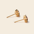 A pair of gold crown stud earrings with small multicolored gemstone accents, displayed on a light beige background.