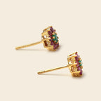 A pair of gold cluster stud earrings featuring a central green oval stone surrounded by small pink and green stones, set in a gold halo with post backs, shown on a light beige background.