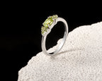 A silver ring with a marquise-cut peridot center stone and small round accent stones, displayed on a textured white stone against a black background.