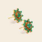A pair of gold cluster stud earrings featuring round green gemstones, arranged on a light beige background.