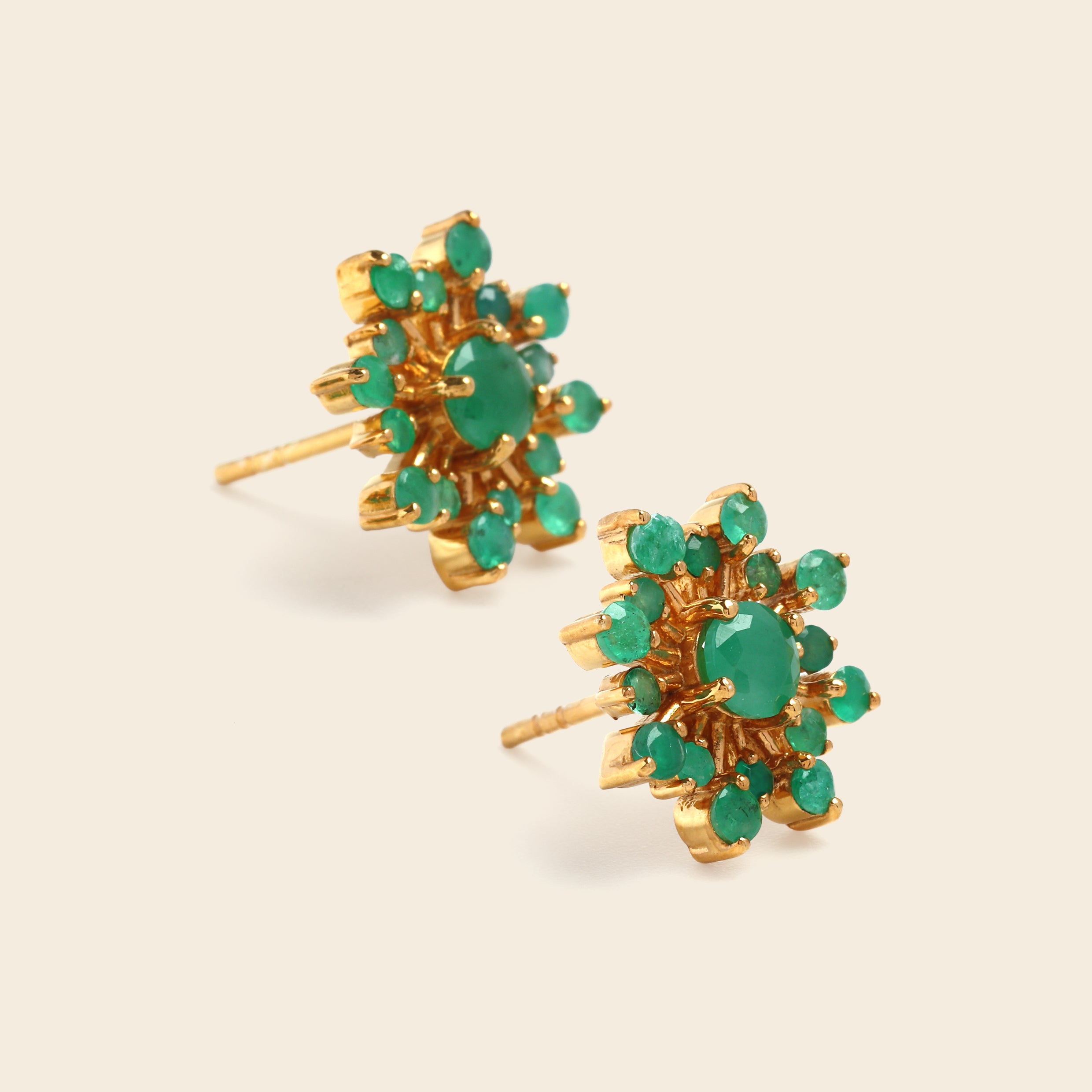 A pair of gold cluster stud earrings featuring round green gemstones, arranged on a light beige background.