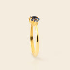 A gold ring with a central dark blue oval gemstone, shown in a side profile against a light beige background.