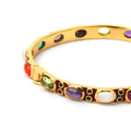 Gold tone bangle with colorful gemstones and red enamel accents, elegant statement jewelry piece