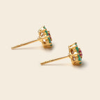 A pair of gold post earrings with a circular cluster setting featuring green and pink gemstones, displayed on a light beige background.