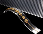 A gold chain bracelet with oval links, each set with small yellow stones, displayed on a clear curved acrylic stand against a black background.