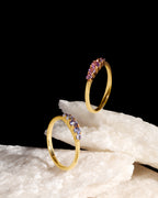 Two gold rings with small pink gemstone clusters, displayed on white textured stone against a solid black background.
