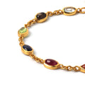 Gold chain bracelet with oval gemstones in green, blue, red, and brown hues, set in polished gold-toned metal.
